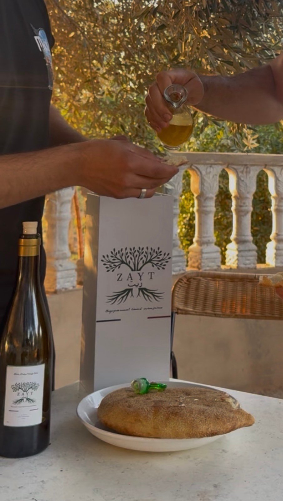 On verse l'huile d'olive Zayt sur du pain, sous les oliviers, à côté de la bouteille et de son coffret